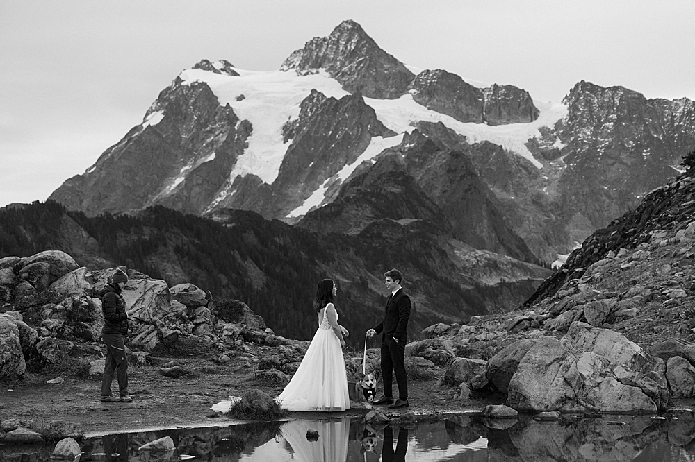Black & white of a bride, groom, and leashed corgi puppy having an elopement ceremony officiated by Adrienne of Wags Down The Aisle at Artist Point.