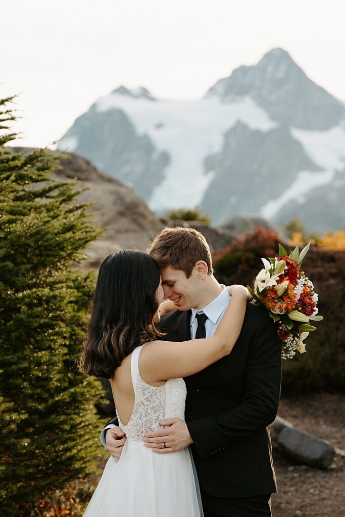 Bride and groom resting foreheads together with a fall colored bouquet draped over the groom's shoulder and Mount Shuksan in the background.