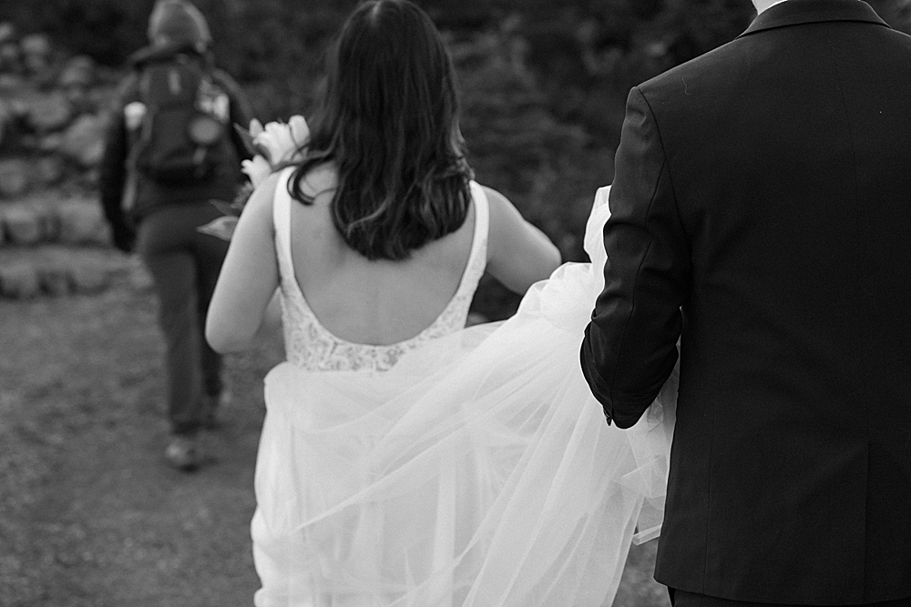 Black & white of groom holding bride's wedding train while walking