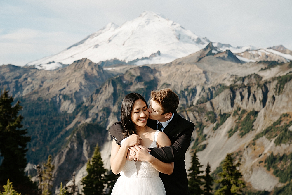Groom kissing bride on the cheek at their sunrise Mount Baker elopement.