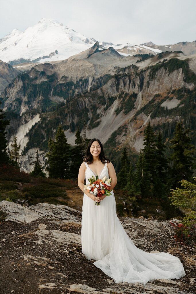 Bride portrait with a long tulle train and fall bouquet standing with views of Mount Baker behind her.