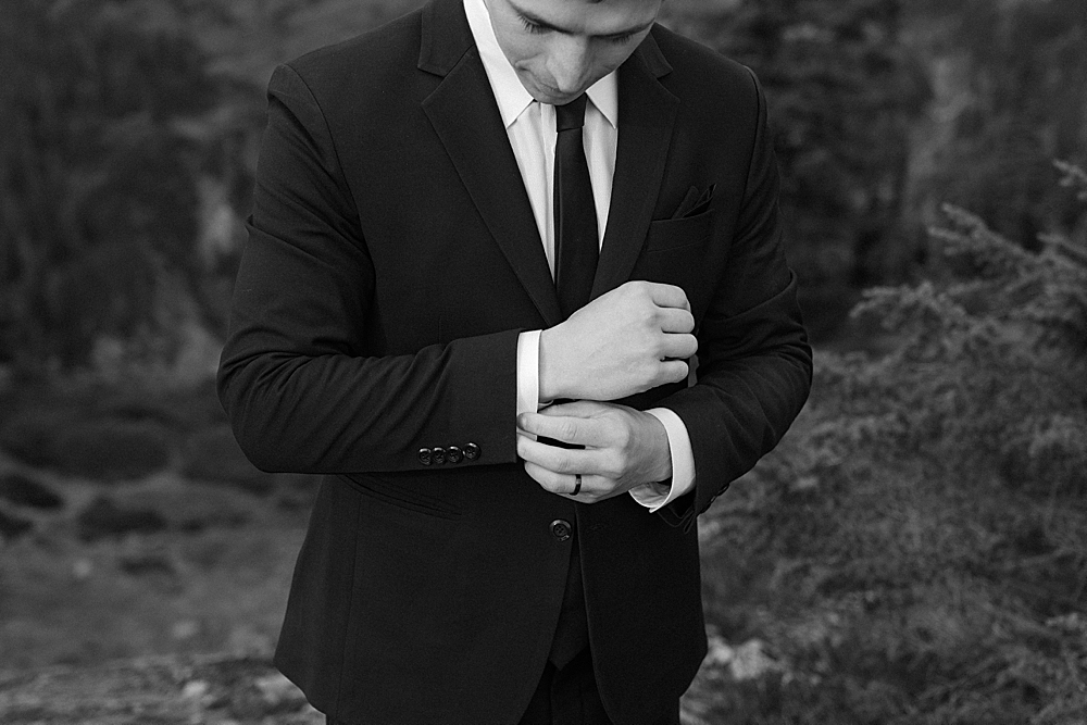 Black & white of groom in a black suit adjusting his sleeves.