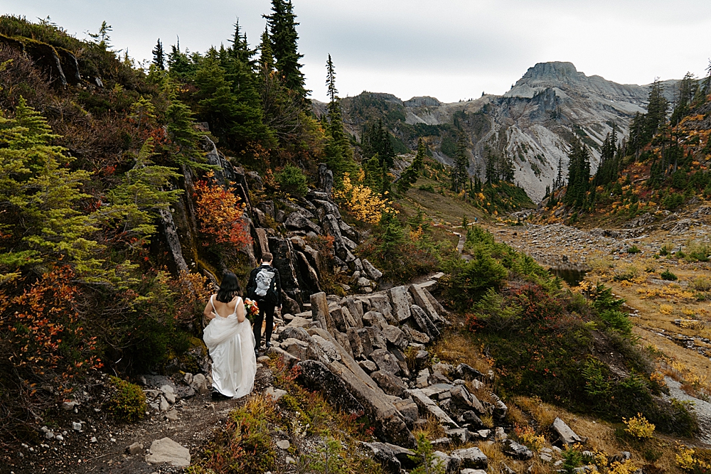 Bride and groom walking on a trail for their PNW fall elopement with lots of gorgeous fall colors around them.