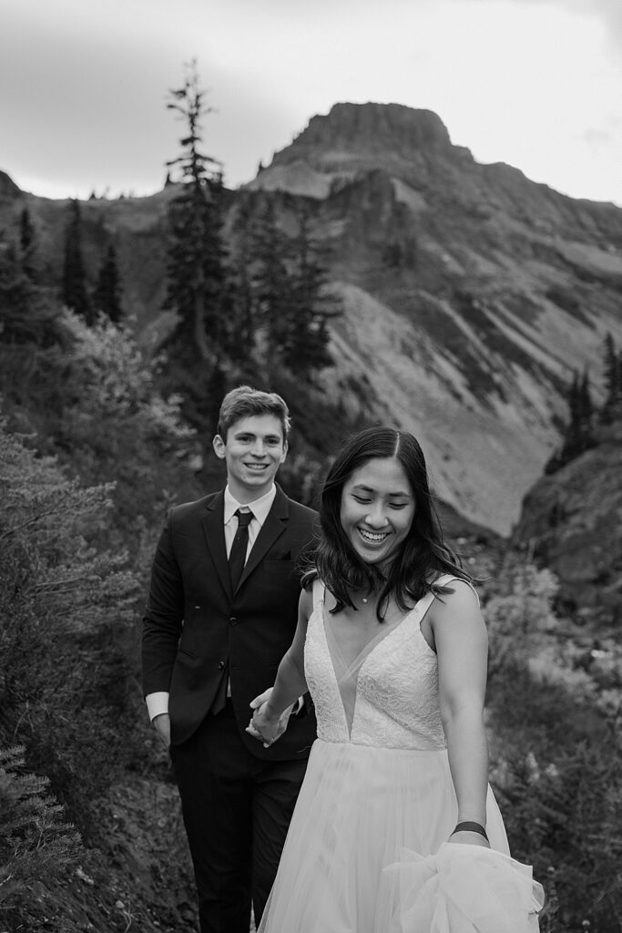 Black & white of bride smiling and holding groom's hand while he smiles at her.