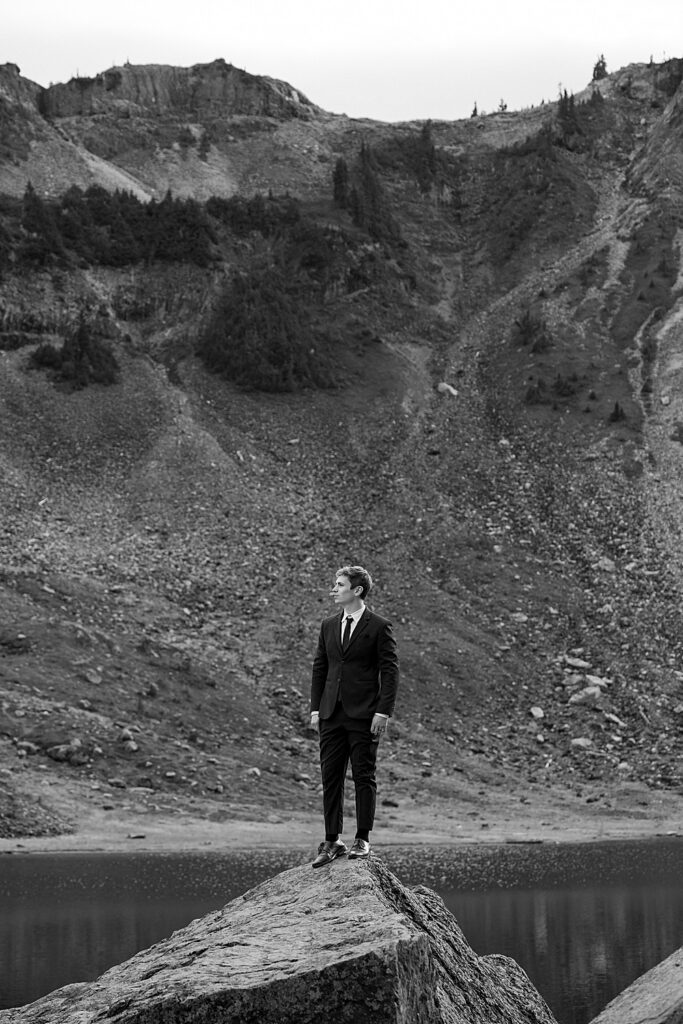 Black & white of groom standing on a rock with mountains in the background