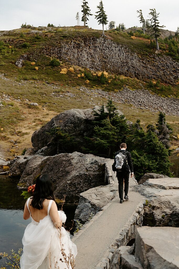 Groom walking across a stone bridge and bride following behind.