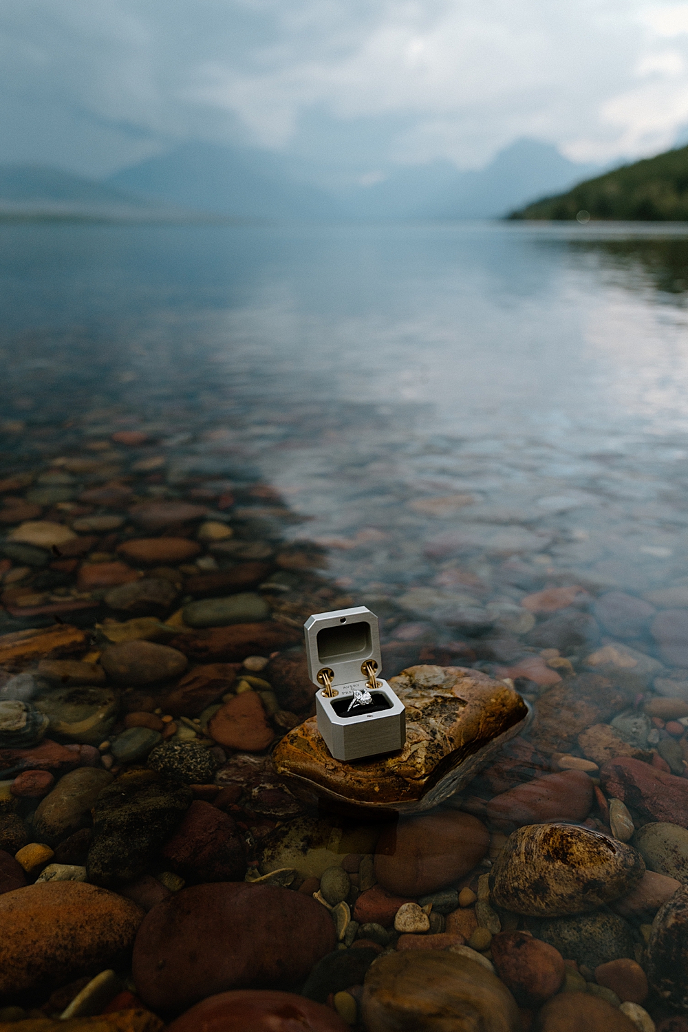 Silver ring box with engagement ring sitting on a rock in Lake McDonald