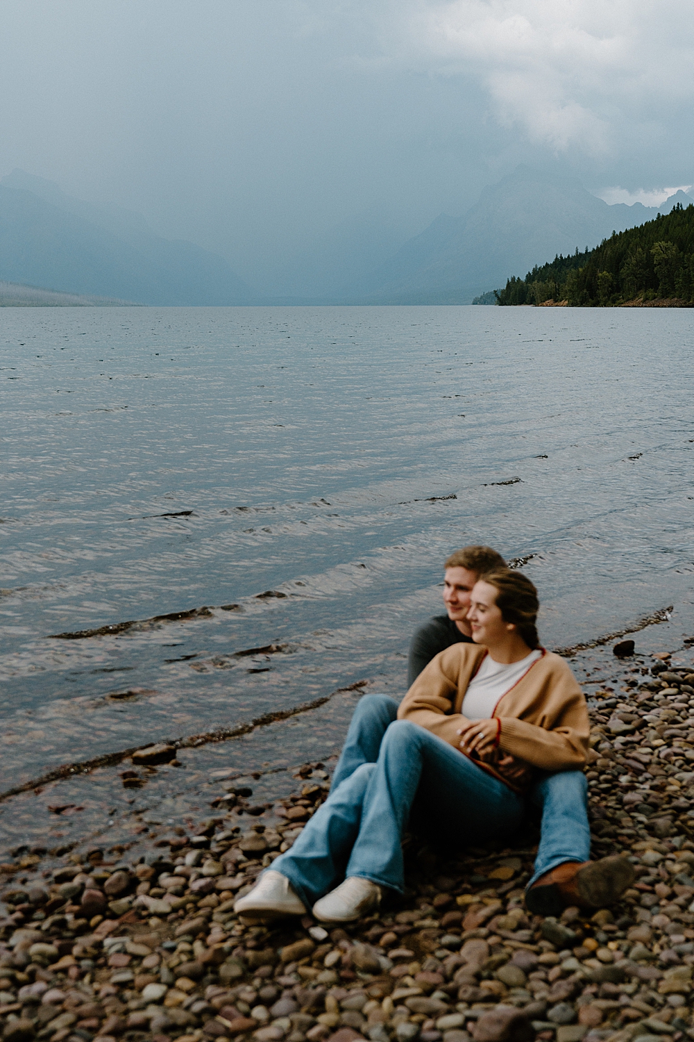 Couple sitting on the rocks at Lake McDonald with a cloudy sky in the background