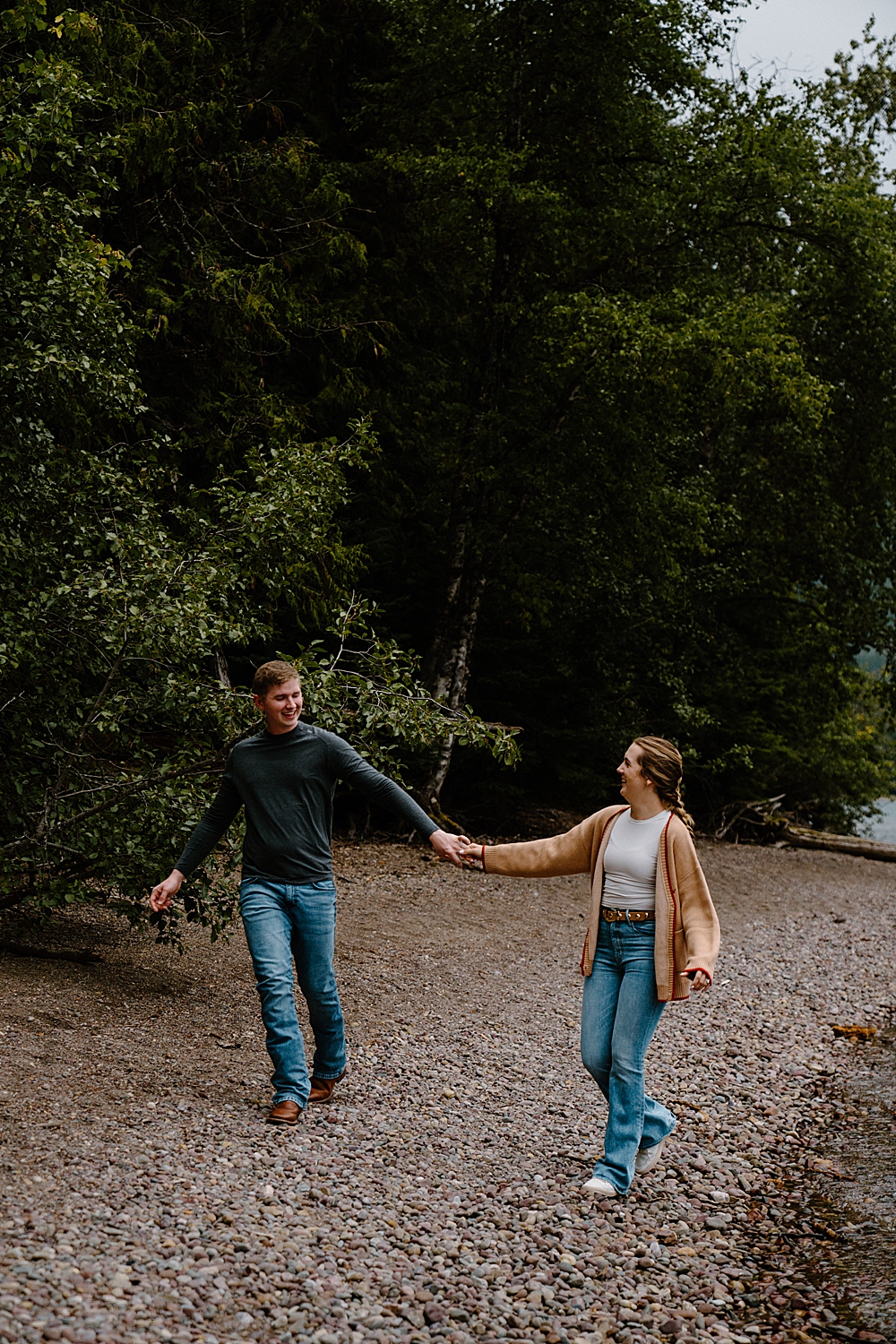Couple holding hands and walking on the beach in Glacier Park for their engagement photos