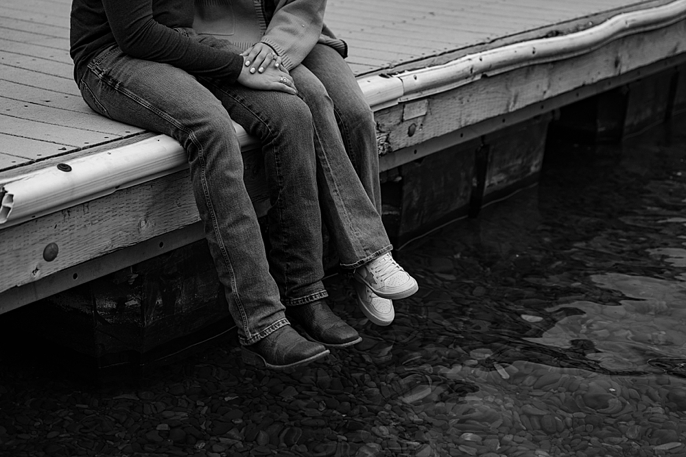 Black & white of couple sitting on a dock with just their hands and legs in the frame