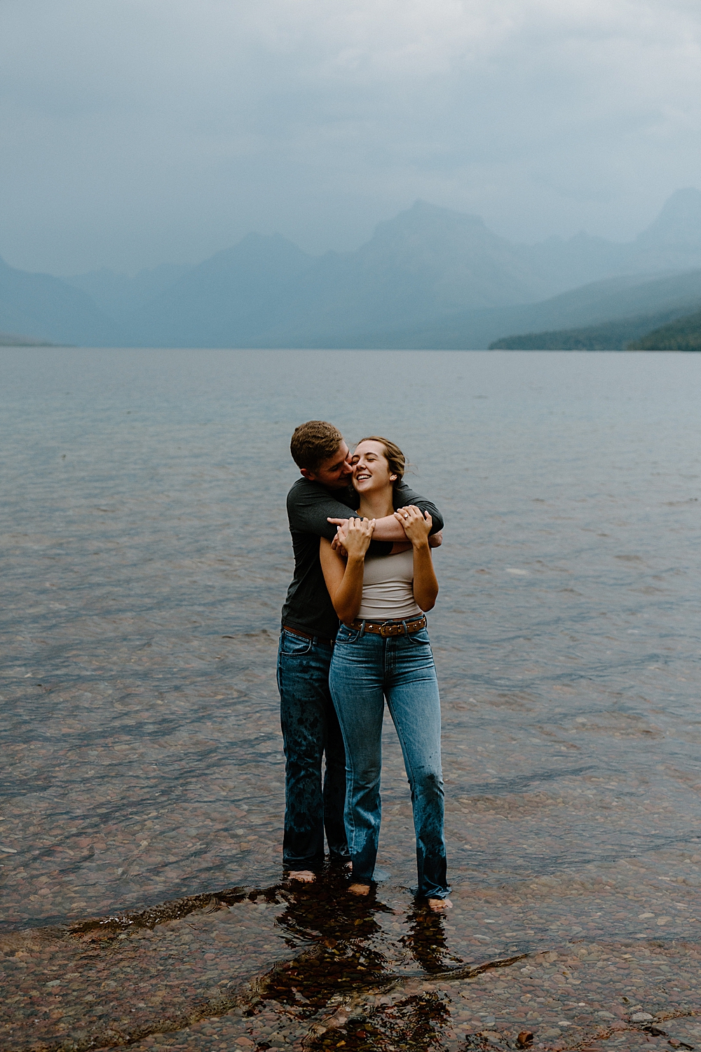 Couple standing in the water at Lake McDonald during their moody evening engagement session with Montana photographer, vVnture to Elope.