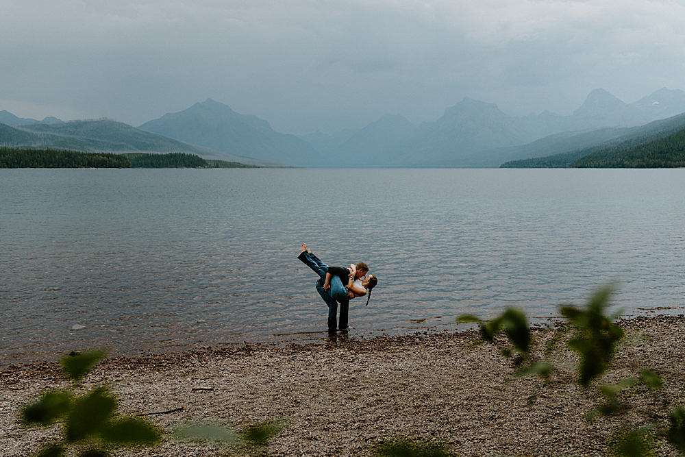 Fiancé dipping his girl while standing in Lake McDonald on a moody evening