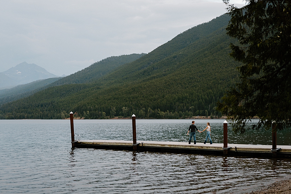 Couple holding hands and walking on dock at Apgar Beach for their Lake McDonald engagement session in Montana