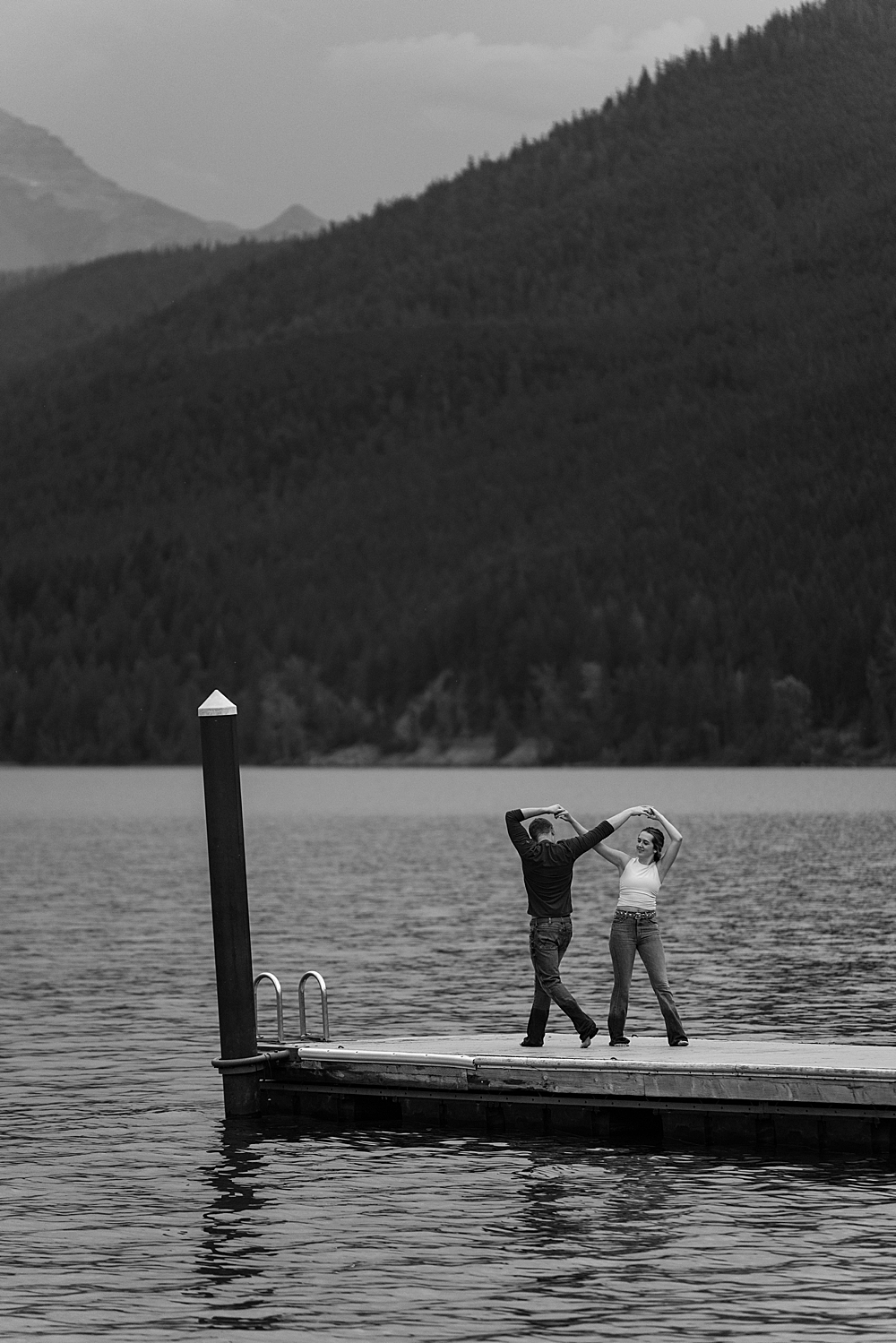 Black & white of couple swing dancing on dock at Apgar Beach for their Lake McDonald engagement session in Montana